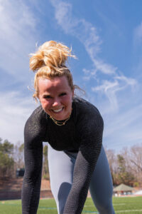 Macy Tartlon bends down towards camera while smiling during an exercise. 