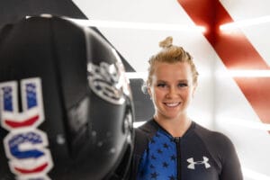 Image of Macy Tarlton wearing a Team USA Uniform and holding up a helmet to the camera. 